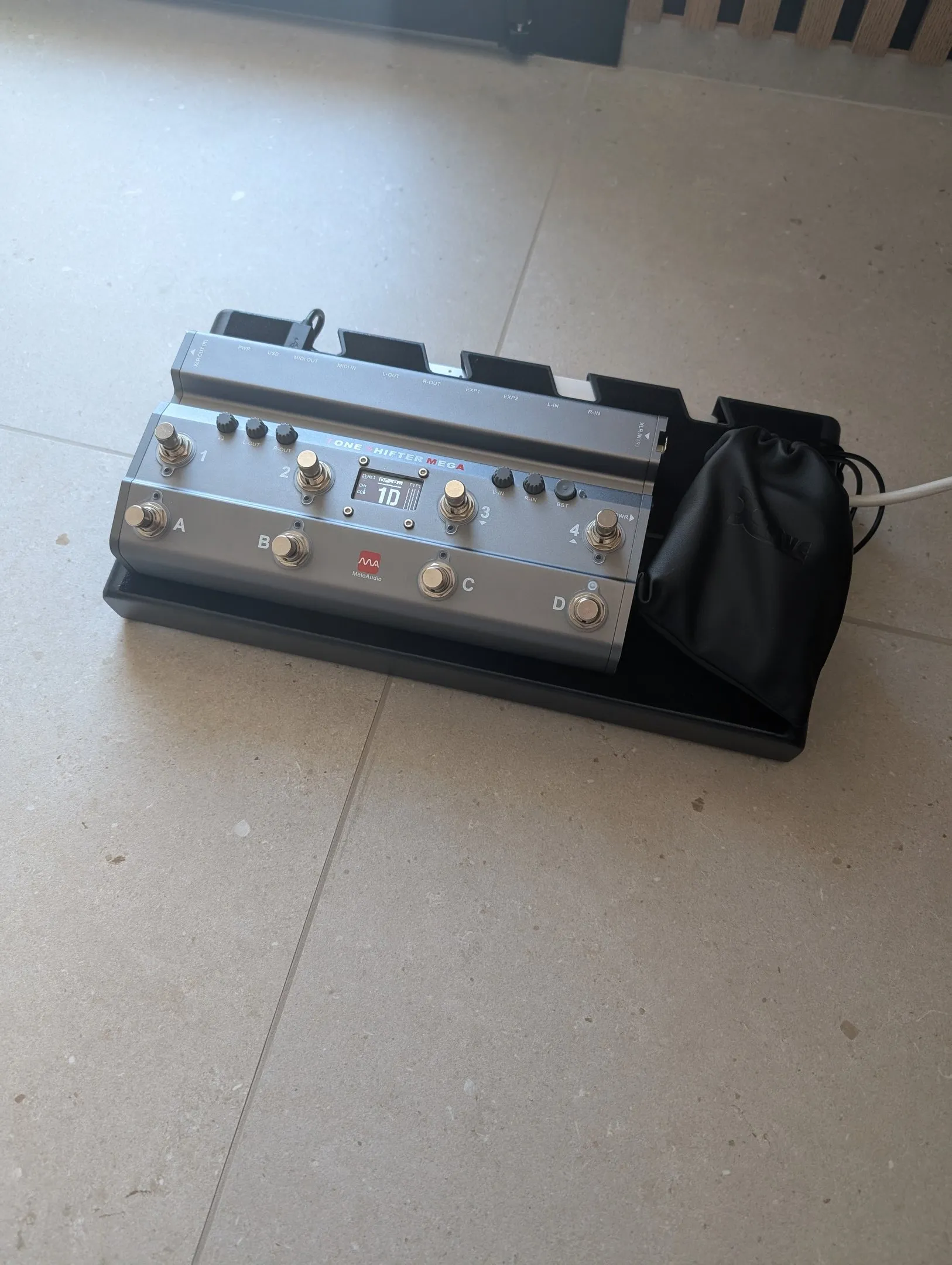 A multi-effects guitar pedalboard on a concrete floor, next to its padded carry bag
